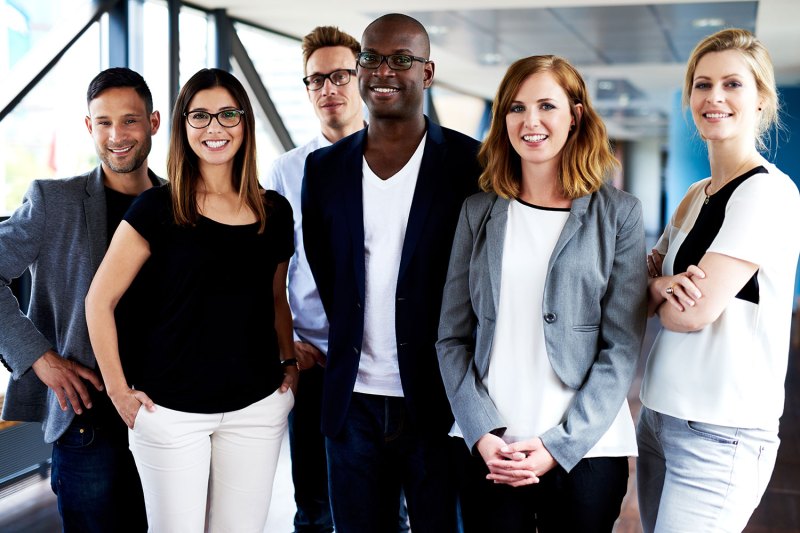 Group of young executives standing, smiling at camera and posing for picture